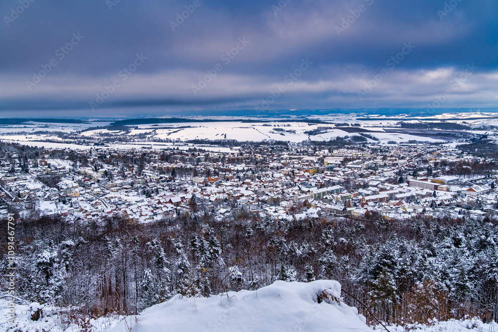 A snowy landscape with a town in the distance. The sky is cloudy and the snow is covering the ground. Germany.