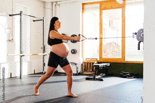 Pregnant Chinese Woman Exercises With Resistance Cable in a Gym, Promoting Health and Wellness During Pregnancy