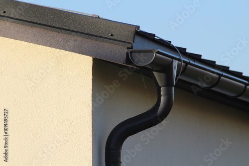 Black gutter on the side of modern white house with black metal roof and small bird sitting on top of the roof. Real estate concept

