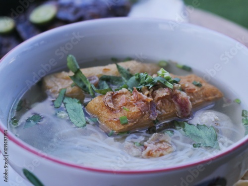 Meatballs with fried tofu in a bowl with clear sauce and vermicelli noodles