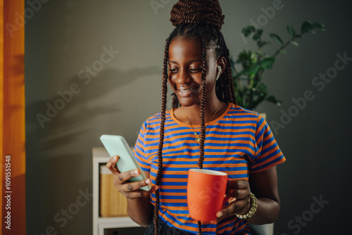 Young woman using mobile phone and drinking coffee at home