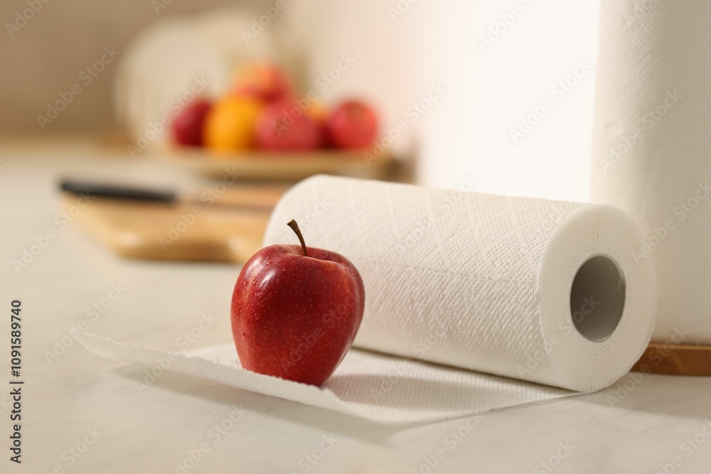 Fototapeta premium Roll of paper towels and red apple on white countertop in kitchen, closeup