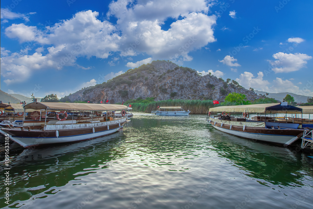 The rock-cut temple tombs of the ancient city of Kaunos in Dalyan, Muğla, Turkey. Beautiful view of Dalyan river with reed beds, excursion boats and carved tombs in the background.