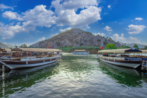 The rock-cut temple tombs of the ancient city of Kaunos in Dalyan, Muğla, Turkey. Beautiful view of Dalyan river with reed beds, excursion boats and carved tombs in the background.