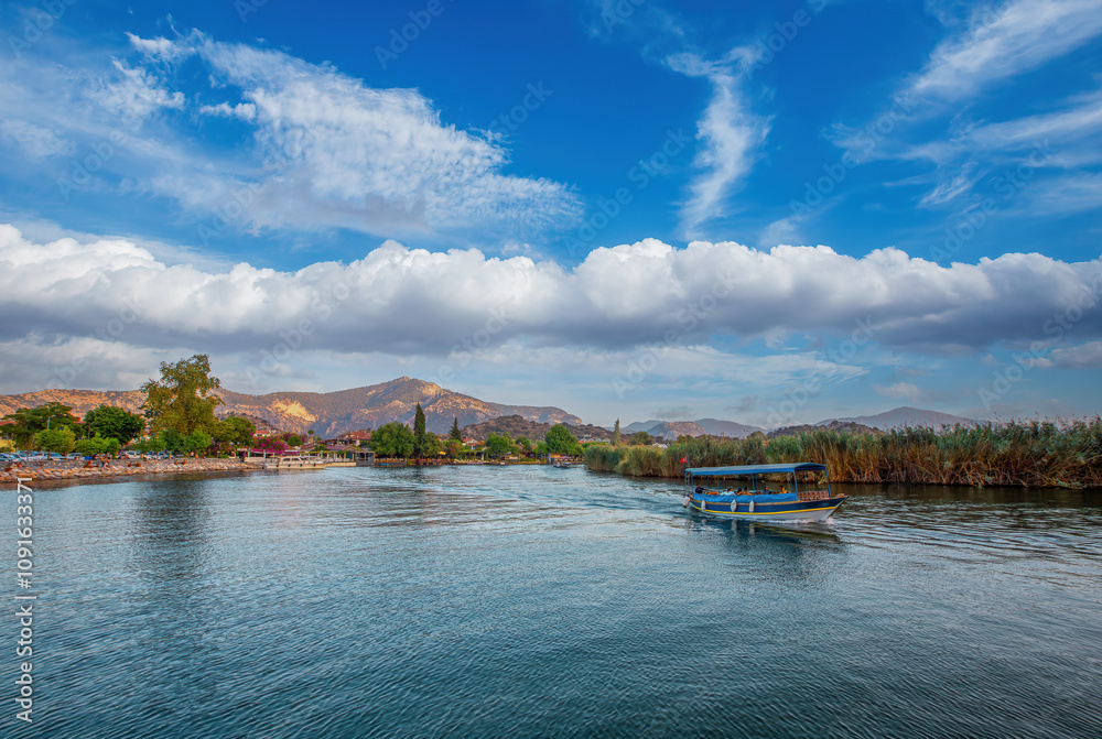 The rock-cut temple tombs of the ancient city of Kaunos in Dalyan, Muğla, Turkey. Beautiful view of Dalyan river with reed beds, excursion boats and carved tombs in the background.