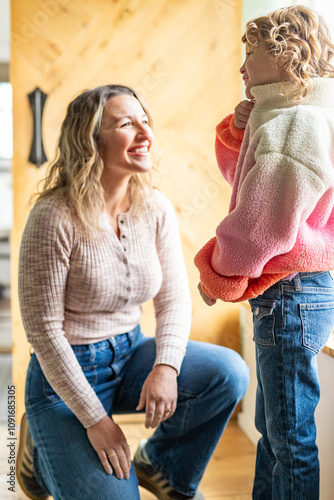 Little girl zipping up jacket with mom smiling