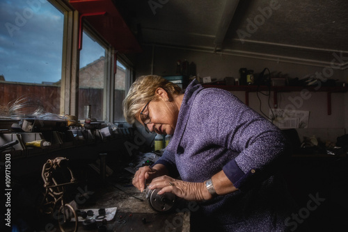 A mature woman restoring a vintage motorcycle in a garden shed workshop.