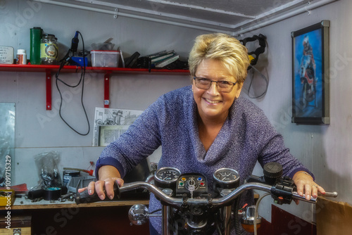 A mature woman restoring a vintage motorcycle in a garden shed workshop.