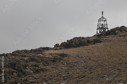 Landscape of the hilly rocky steppe in fade autumn colors in Mongolia. A place similar to the lands of the Orcs. On the peak of a hill is a wooden military signal construction like a cell.
