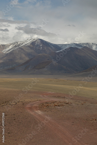 Long curved country road running along the hilly steppe. Road lead to the mountains ridge in the distance. Golden autumn roadscape: endless expanses, emptiness, abandoned and deserted territory.