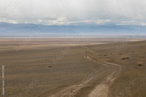 Long curved country road running along the hilly steppe. Road lead to the mountains ridge in the distance. Golden autumn roadscape: endless expanses, emptiness, abandoned and deserted territory.