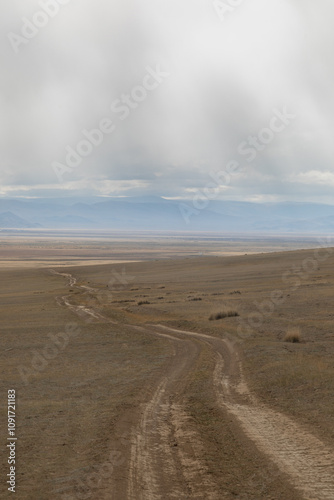Long curved country road running along the hilly steppe. Road lead to the mountains ridge in the distance. Golden autumn roadscape: endless expanses, emptiness, abandoned and deserted territory.