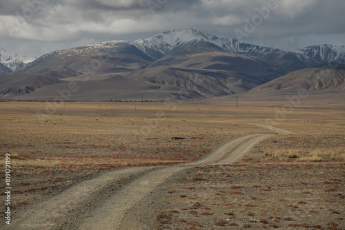 Long curved country road running along the hilly steppe. Road lead to the mountains ridge in the distance. Golden autumn roadscape: endless expanses, emptiness, abandoned and deserted territory.