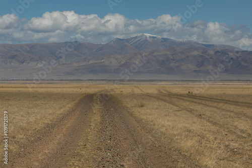 Long curved country road running along the hilly steppe. Road lead to the mountains ridge in the distance. Golden autumn roadscape: endless expanses, emptiness, abandoned and deserted territory.