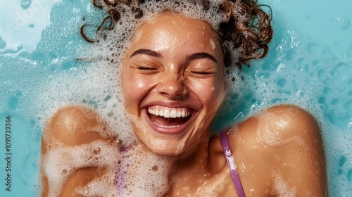 A joyful woman with curly hair laughing heartily while submerged in a bath filled with soapsuds, radiating happiness and relaxation in a playful setting.