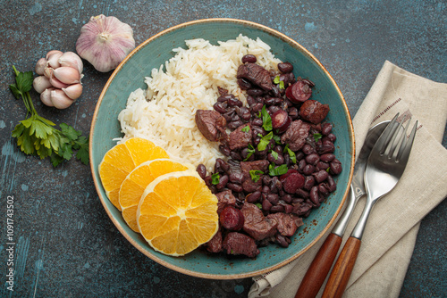 Fototapeta Naklejka Na Ścianę i Meble -  Feijoada, a hearty brazilian stew, with white rice and orange slices, showcasing a vibrant culinary tradition of Brazil alongside garlic and parsley