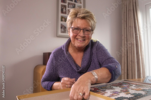 A mature retired woman completing a jigsaw in a small domestic dining room.