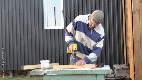 Adult man rolls up an electric wire.
Electrician. Construction work. Countryside plot. Open. Evening time. Real time.