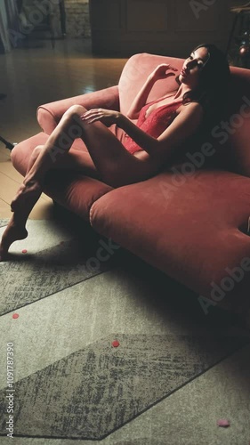 Beautiful brunette posing sexy on camera in red lace bodysuit while sitting on sofa