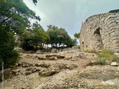 Historic Pic Saint-Loup Chapel Surrounded by Rugged Limestone Rocks and Lush Greenery Under a Cloudy Sky in Southern France photo