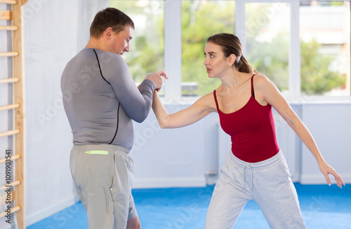 Aggressive young girl and middle-aged man practicing arm twist technique during self-defense courses photo