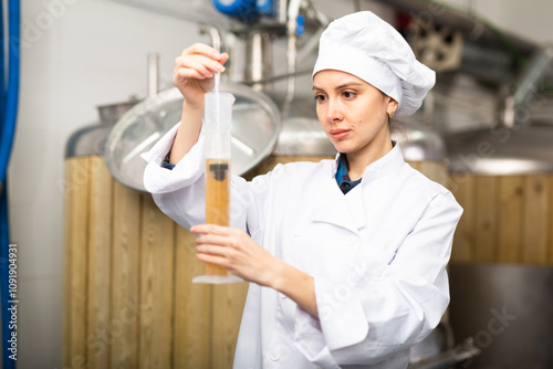 Woman brewmaster in white coat measuring beer sample with alcoholometer. photo