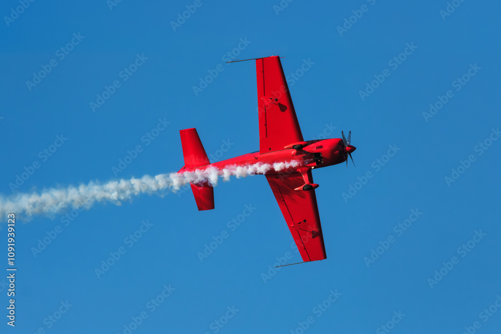 Fototapeta premium Red stunt aerobatic plane performing stunts in blue sky. Concept of speed, difficulty, precision, risk