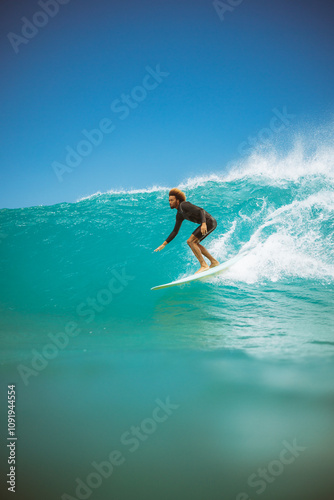 A surfer is riding a wave in the ocean. The surfer is wearing a black wetsuit. The ocean is calm