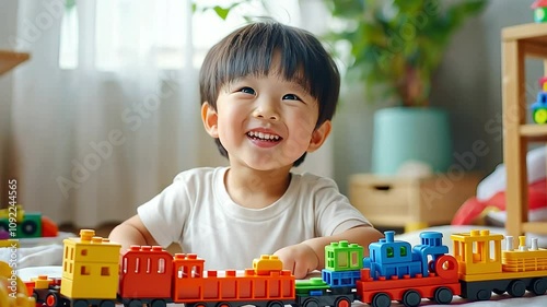 A happy Asian kindergartener is having fun playing with a colourful train block toy in the white lesson room. photo