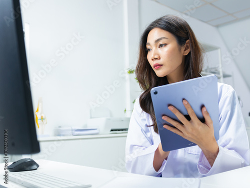 Asian female doctor reviewing medical data on a digital tablet focused on diagnosis and treatment planning in a modern clinic. Young Asian doctor concentrating on patient data and medical report.