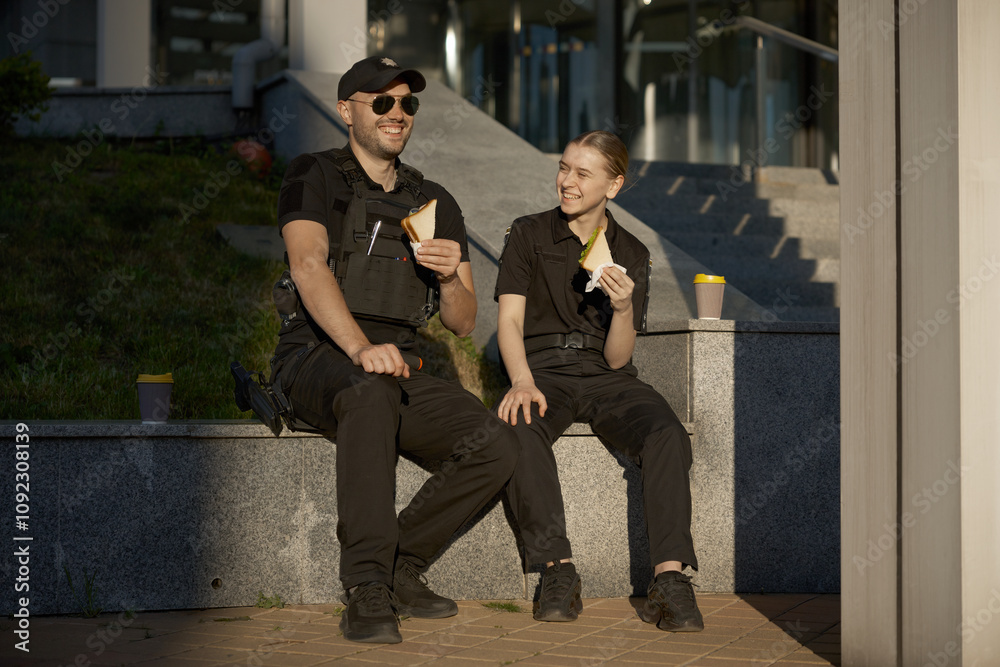 Fototapeta premium Smiling male and female patrol police officers enjoying lunch break outdoor