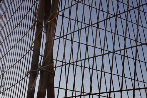 closed metal grid on roof of iron fence against blue sky, metal structure with grille lattice. Steel lattice against heaven. wire fence. Fence grilles rust texture background. Fence Steel Background. photo