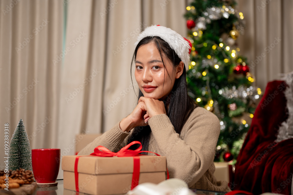 A charming Asian woman in cozy clothes sits at a coffee table with a Christmas present box. A charming Asian woman in cozy clothes sits at a coffee table with a Christmas present box.