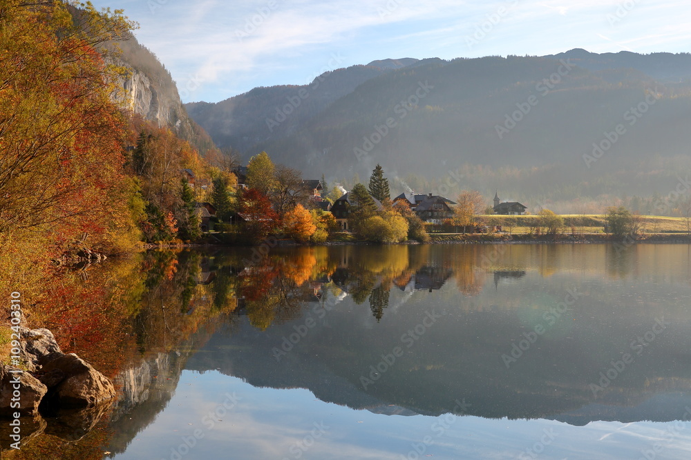 Colorful Autumn scenery on a misty morning and reflections on the Grundlsee lake (Eastern part), Salzkammergut, Styria, Austria, Europe, with the village Gossl