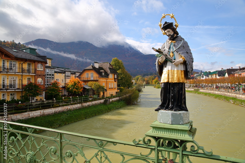 The painted statue of Saint John of Nepomuk (erected in 1900), located on the Elisabeth Bridge over the river Traun in Bad Ischl, Salzkammergut, Styria, Austria, Europe, with heritage buildings on the