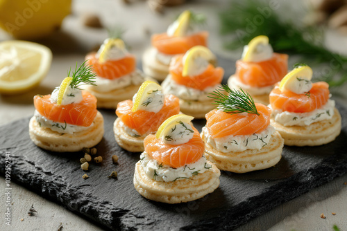 Mini smoked salmon blinis topped with cream cheese, dill, and a tiny lemon twist, arranged on a slate platter photo