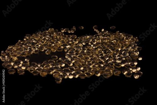 A large number of soft gel supplements arranged on a sleek black surface. The glossy capsules reflect light beautifully, emphasizing their texture and vibrant color.