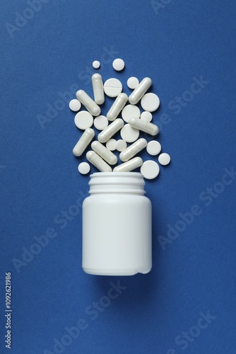 Various pills pouring out of a medicine bottle on color background photo