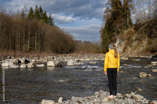 Woman or Girl in yellow anorak standing on a rock looking into the wild nature of the Bregenzerwald on the river Bregenzer Ache