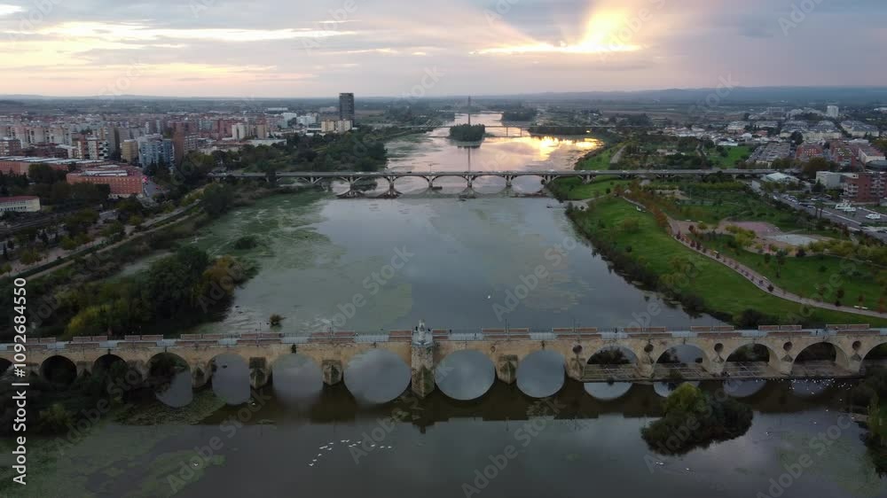 Palmas Bridge, University Bridge, And Puente Real Spanning Guadiana River At Sunset In Badajoz, Spain. aerial orbiting Palmas Bridge, University Bridge, And Puente Real Spanning Guadiana River At Sunset In Badajoz, Spain. aerial orbiting