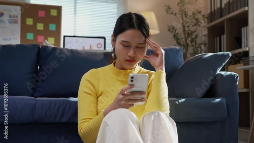 Freelancer feeling frustrated while staring at her smartphone screen, expressing stress and concern in a home office setting