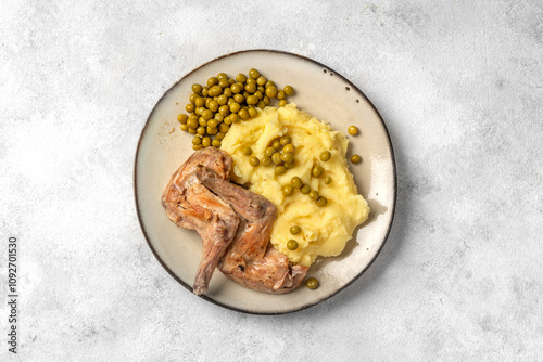 Pieces of rabbit stew, mashed potatoes and green peas on a plate on a on a light gray table top view
