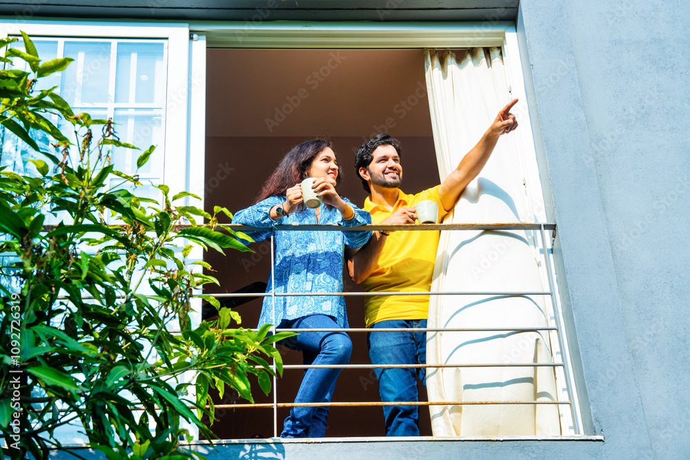 Indian couple in their thirties enjoying coffee and conversation on balcony in morning sun