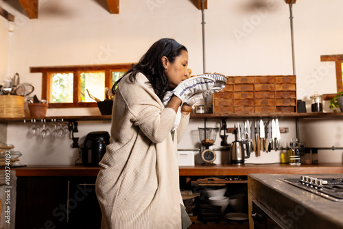 Senior woman in cozy kitchen smelling freshly baked pie with oven mitts, at home photo