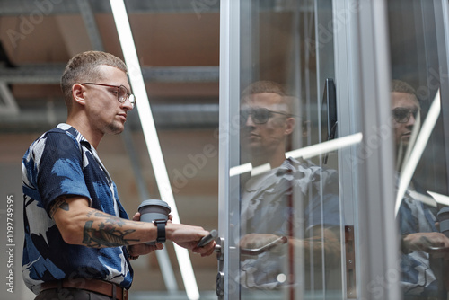 Side view of modern businessman opening door holding reusable cup with coffee while walking into office room in coworking, copy space