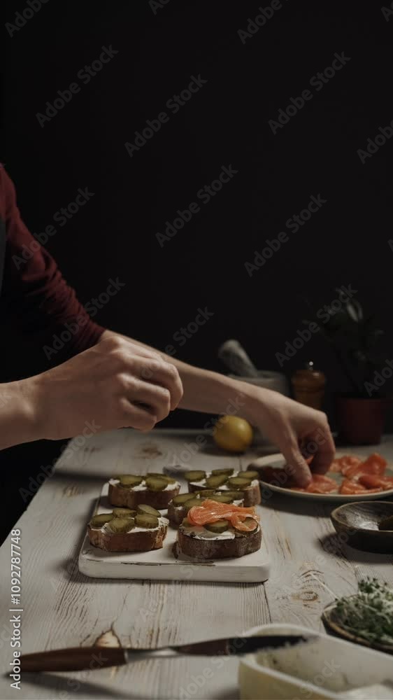 Hands close-up, put slices of smoked salmon on bread with cream cheese and pickled cucumber Hands close-up, put slices of smoked salmon on bread with cream cheese and pickled cucumber