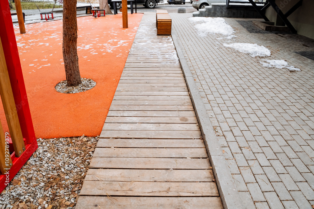 Obraz premium A wooden walkway gracefully directs visitors towards a playground that is located at the center, with a beautiful tree standing tall in the middle, creating a natural setting for play