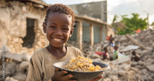 Young refugee vagabond boy holding a bowl of rice and smiling in front of destroyed buildings photo