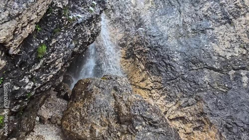 Slow motion video of a mountain stream cascading among rocky formations as the first snowflakes of winter fall gently into the camera’s view, creating a serene and meditative atmosphere