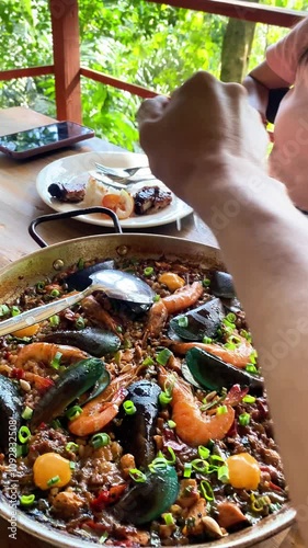 paella with seafood, mussels and shrimp served in a restaurant, a hand squeezes lemon juice onto the food